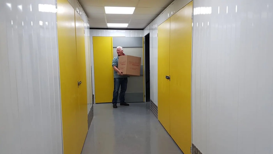A customer carrying a box along a clean corridor of yellow-doored storage rooms